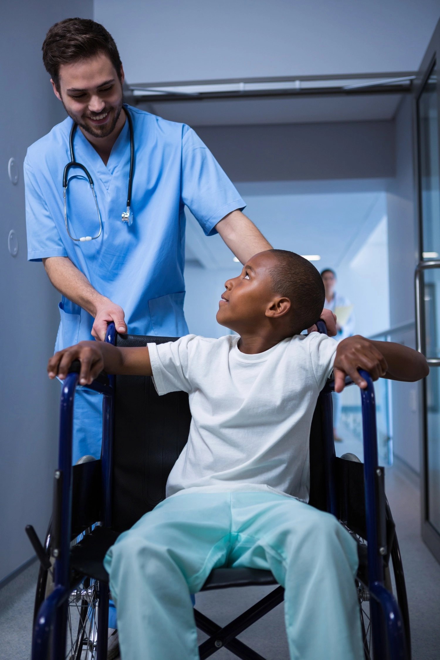 Young child in wheelchair being pushed by nurse