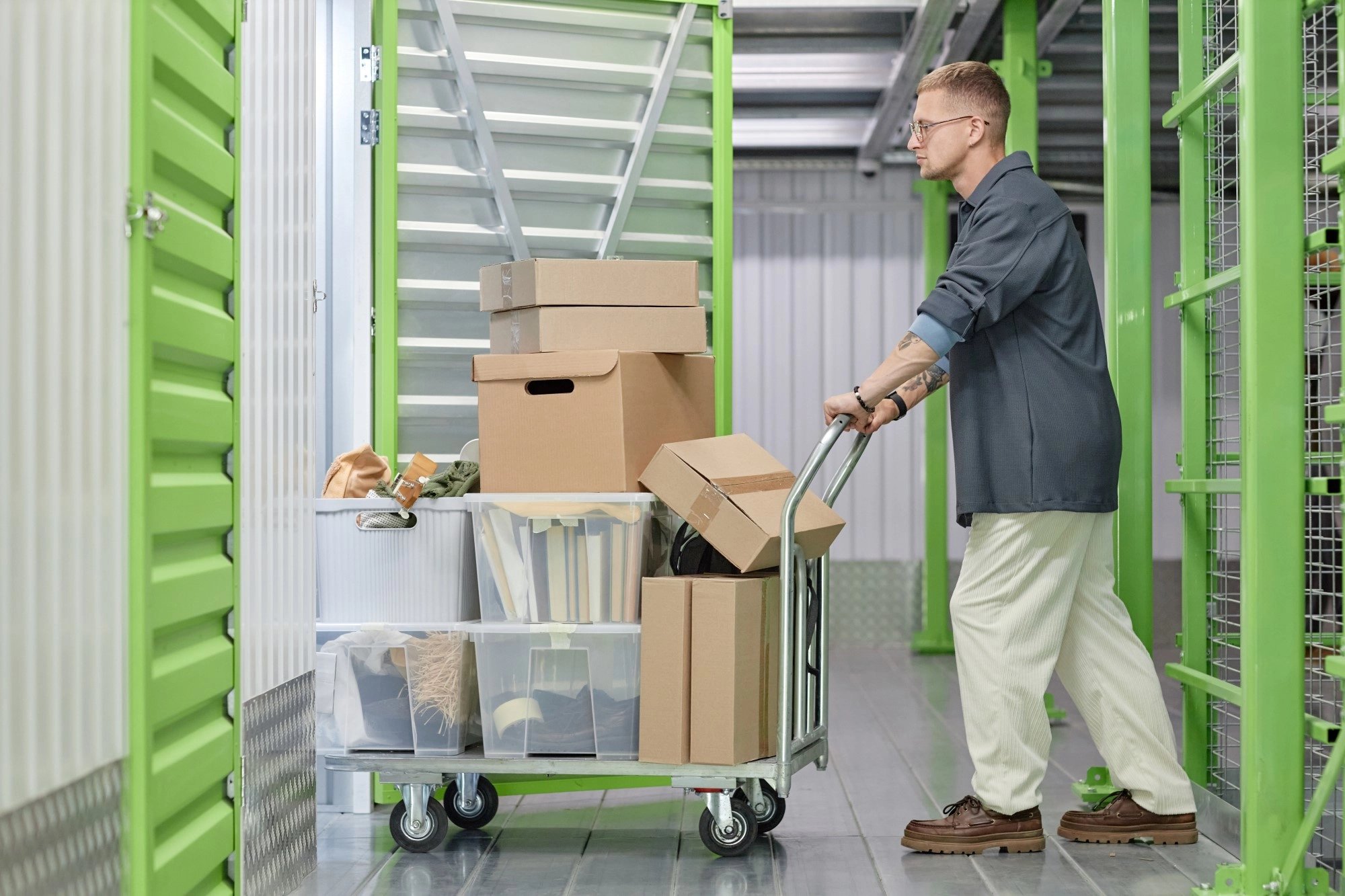smiling-female-client-loading-boxes-into-self-storage-unit-using-cart-warehouse