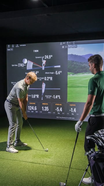 Golf coach pointing at swing data on an impact screen with a student watching.