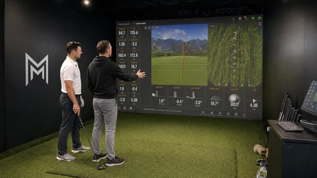 Golfer studying swing telemetry on a wall-mounted analytics monitor.
