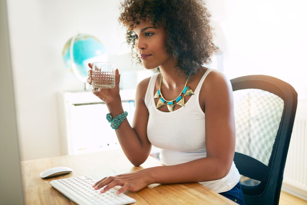 une femme boit un verre d'eau assise à son bureau