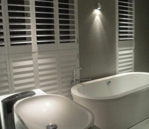 Modern bathroom with white shutters, freestanding tub, and vessel sink. 