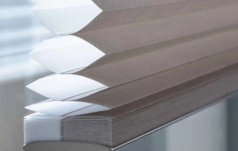 Close-up of beige cellular shades, also known as honeycomb blinds, stacked neatly.