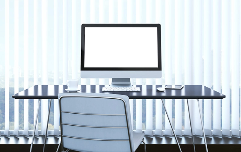 Modern desk setup with computer and office chair in front of window blinds.