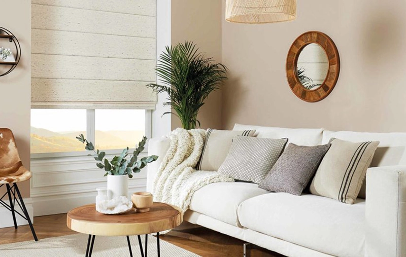 Bright living room with white sofa, round wood coffee table, and neutral Roman shades on the window.