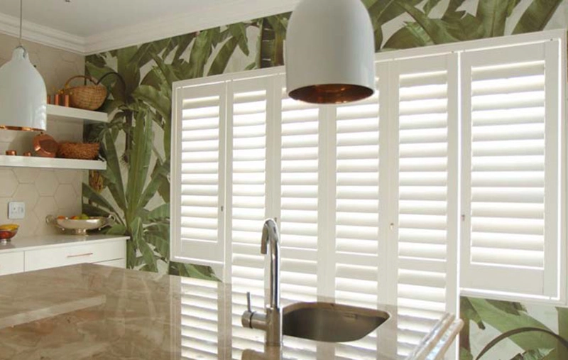 Kitchen with white shutters, tropical wallpaper, pendant lights, and marble countertop.