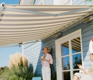 Retractable striped awning shades a patio with a woman and man.