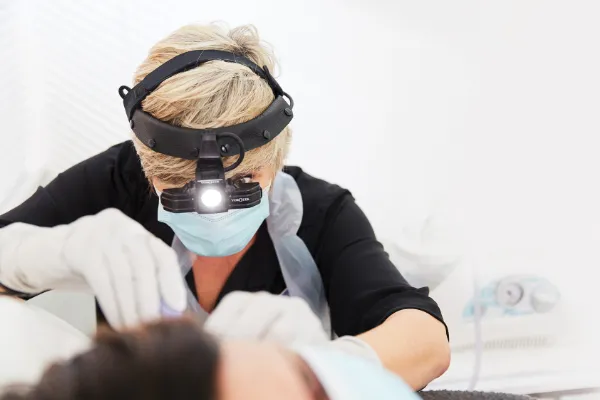 A woman is receiving ear wax removal treatment from a professional practitioner